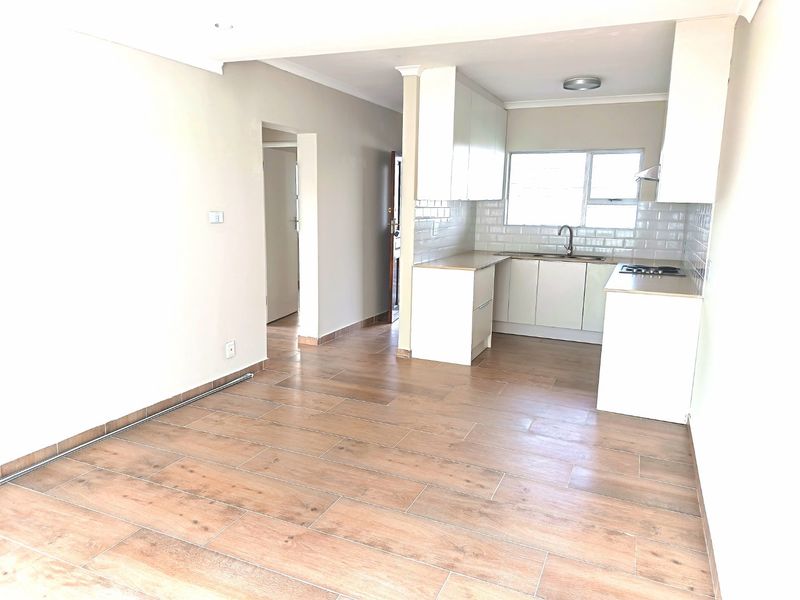 An open-plan living and kitchen area featuring modern wood-look tile flooring, white cabinetry, and a subway tile backsplash in a bright, neutral space.