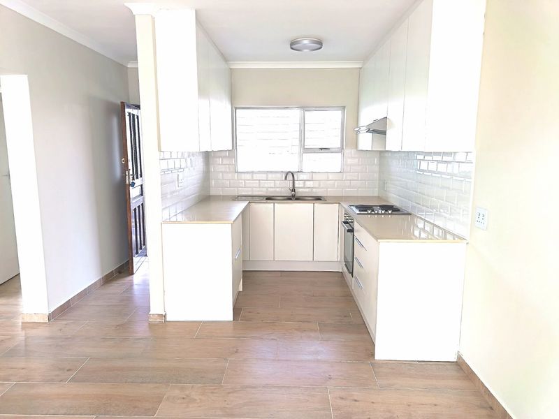 A clean, modern kitchen featuring white cabinetry, subway tile backsplash, stone countertops, and integrated appliances, finished with wood-look floor tiles.