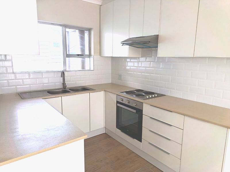 Modern kitchen featuring white cabinetry, subway tile backsplash, built-in oven, electric hob, and stainless steel sink with wood-look flooring.