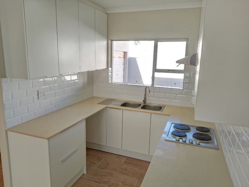 A clean, modern kitchen featuring white cabinetry, subway tile backsplash, stone countertops, and a built-in electric hob with an extractor fan.