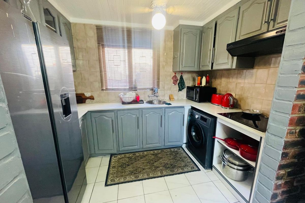 A functional kitchen featuring grey cabinetry, tiled backsplash, built-in hob with extractor fan, and tiled flooring, offering a practical layout for daily cooking.