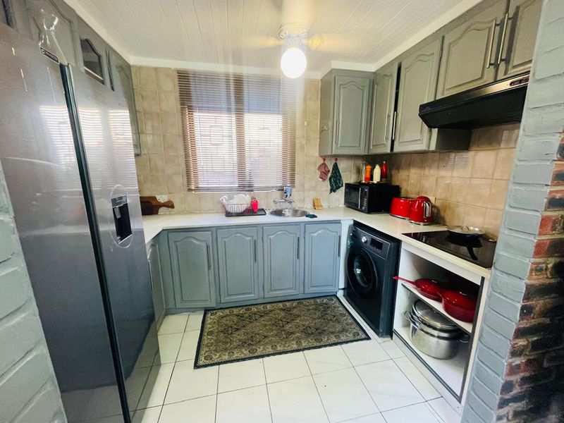A functional kitchen featuring grey cabinetry, tiled backsplash, built-in hob with extractor fan, and tiled flooring, offering a practical layout for daily cooking.