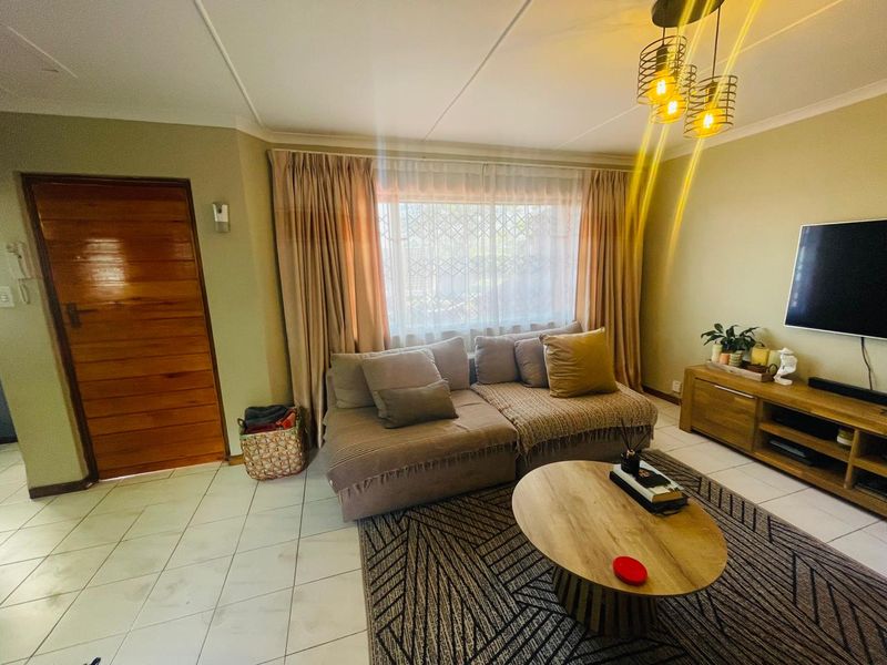 A cozy living room featuring tiled flooring, a wooden door, and a window fitted with security bars, offering a comfortable and functional space.