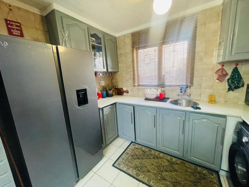 A functional kitchen featuring grey built-in cabinetry, tiled backsplash, laminate countertops, and a stainless steel sink with natural light from the window.