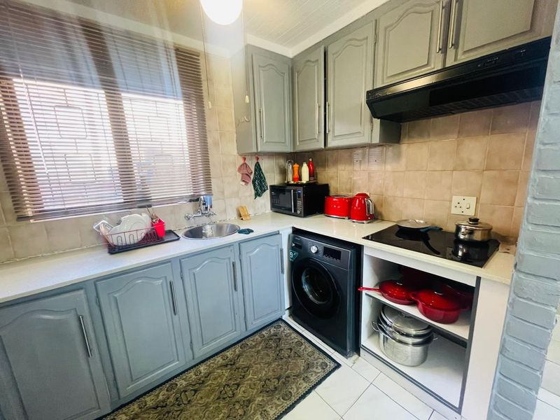 Compact kitchen featuring grey cabinetry, tiled splashbacks, a ceramic hob with extractor fan, and integrated space for a washing machine.