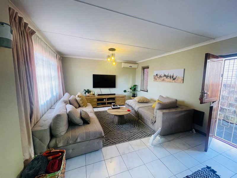A comfortable living room featuring tiled flooring, a wall-mounted air conditioning unit, and direct access to an outdoor area through a timber door.