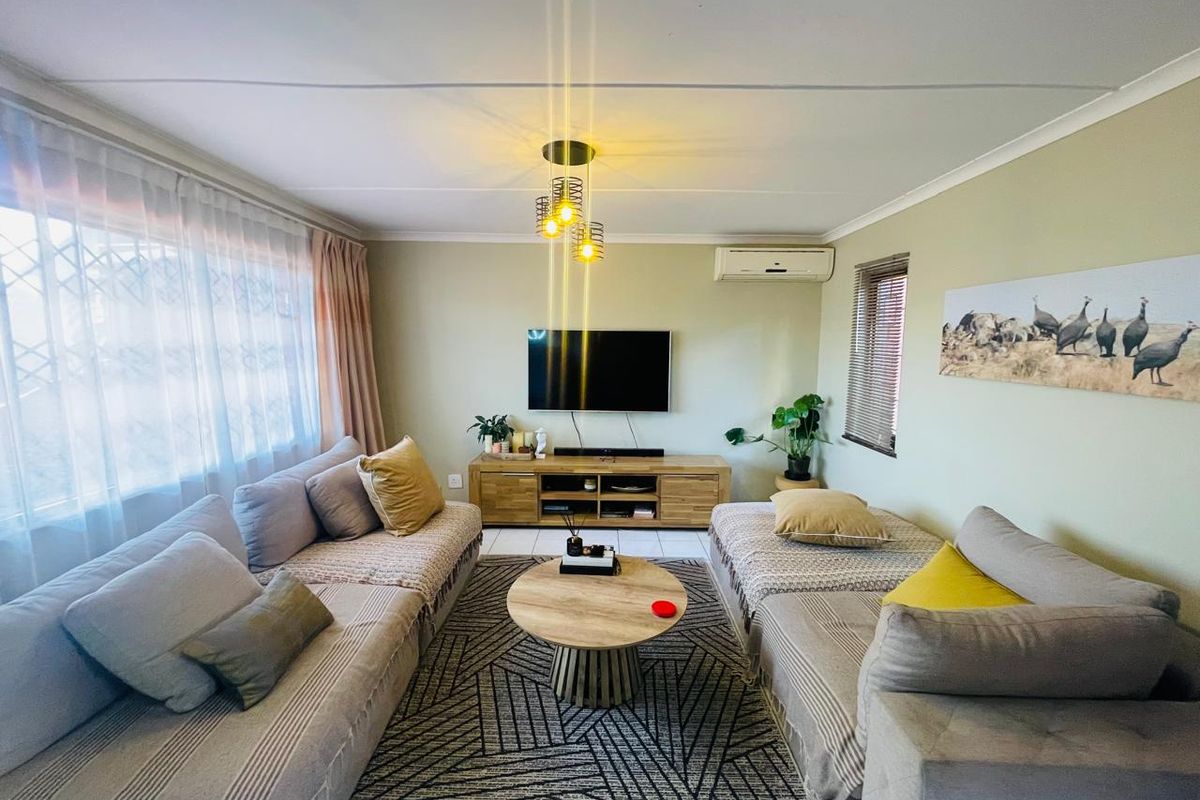 A comfortable living room featuring a split-system air conditioner, neutral wall tones, and large windows with security gates.