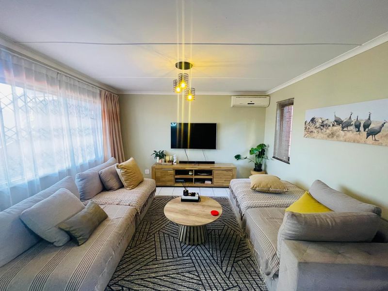 A comfortable living room featuring a split-system air conditioner, neutral wall tones, and large windows with security gates.