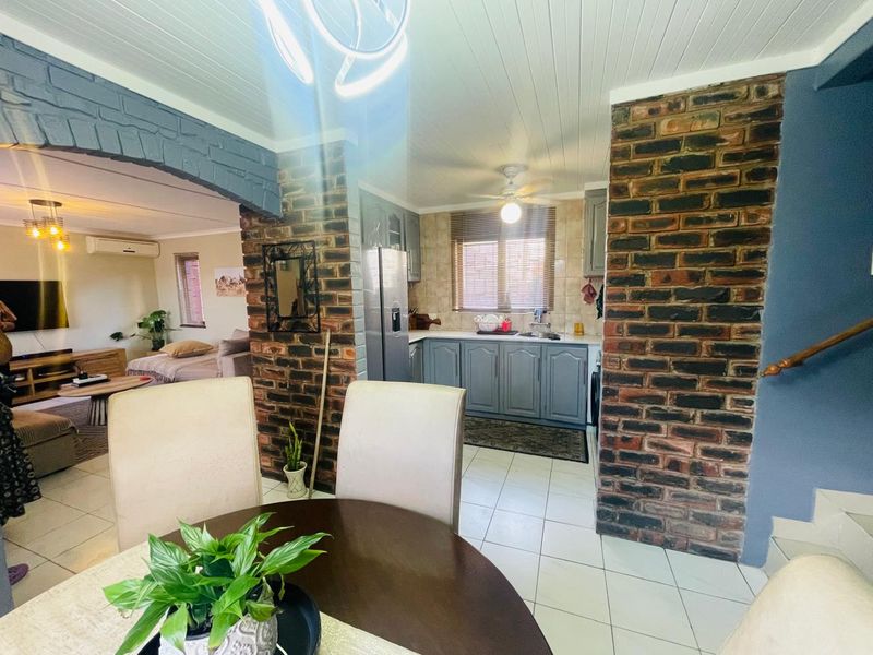 Open-plan living and kitchen area featuring exposed brick pillars, tiled flooring, and functional kitchen cabinetry with a neutral aesthetic.