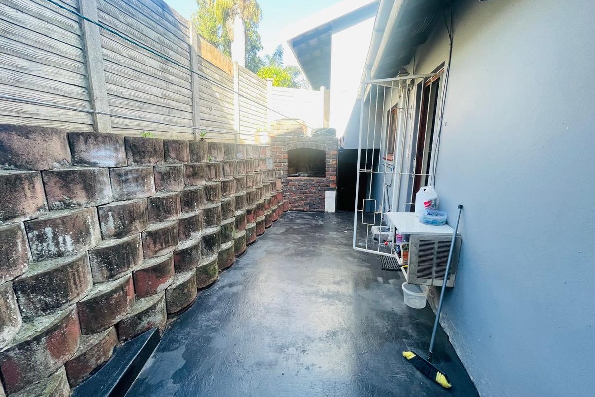A paved rear courtyard featuring a built-in brick braai and a tiered retaining wall, offering a functional outdoor space.