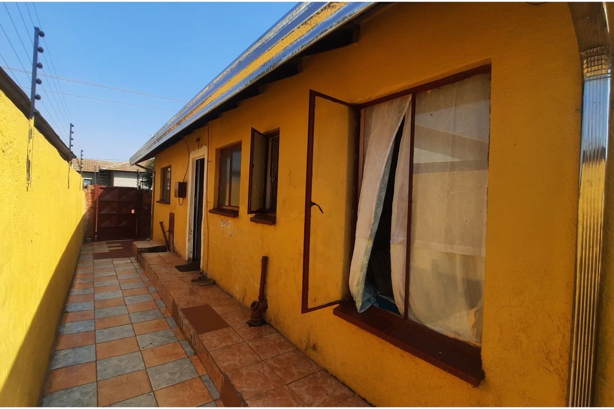 Side exterior view of the property featuring a tiled walkway, yellow painted walls, and security fencing along the boundary.