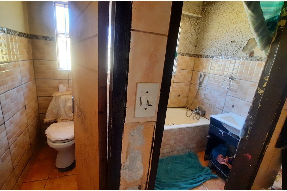 A dated bathroom featuring a bathtub, toilet, and vanity basin, requiring significant renovation and repair to wall finishes and fixtures.