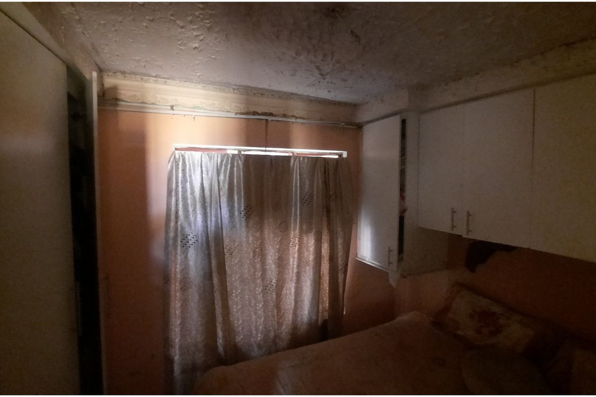 A bedroom featuring built-in cupboards and ceiling cornice, currently requiring significant maintenance and cosmetic updates to the ceiling and wall finishes.