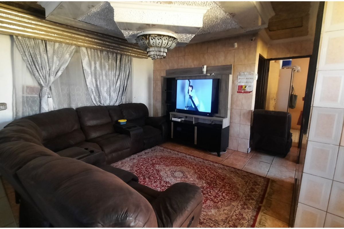 A living room featuring tiled flooring, decorative ceiling molding, and tiled wall accents, currently showing signs of wear and dated finishes.