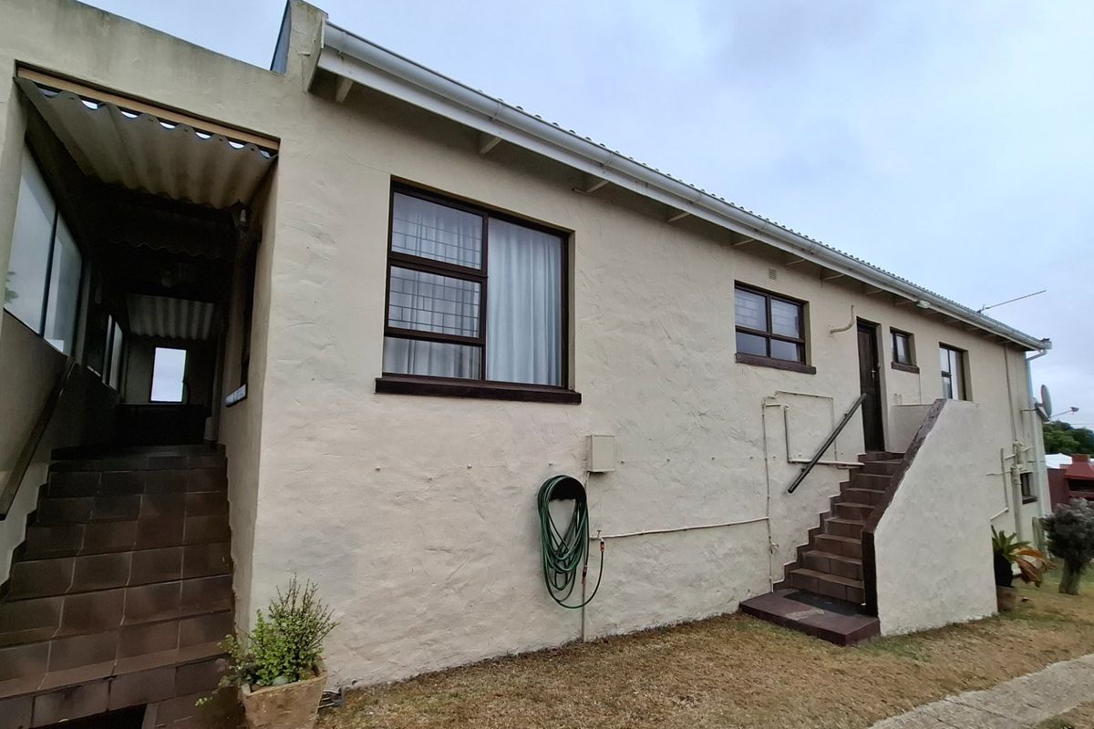Rear exterior view of the property featuring plastered walls, tiled staircases, and metal-framed windows with security bars.