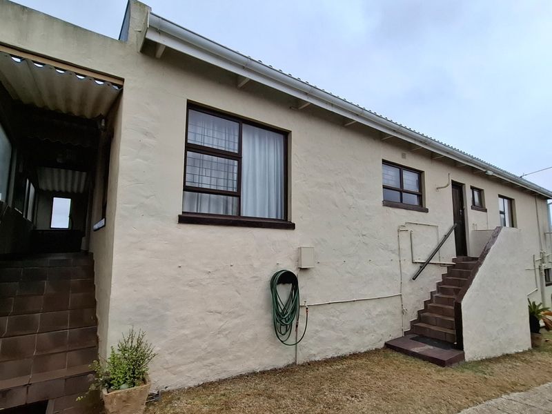 Rear exterior view of the property featuring plastered walls, tiled staircases, and metal-framed windows with security bars.