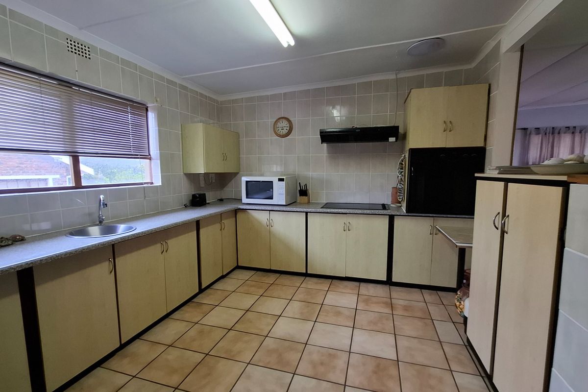 Functional kitchen featuring tiled splashbacks, laminate cabinetry, built-in cooktop, extractor fan, and tiled flooring, offering a practical layout with ample storage space.