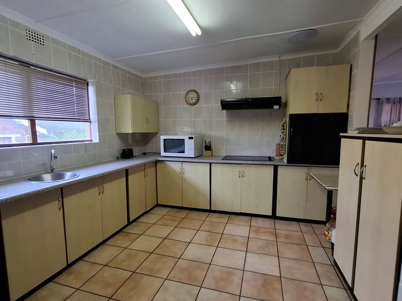 Functional kitchen featuring tiled splashbacks, laminate cabinetry, built-in cooktop, extractor fan, and tiled flooring, offering a practical layout with ample storage space.