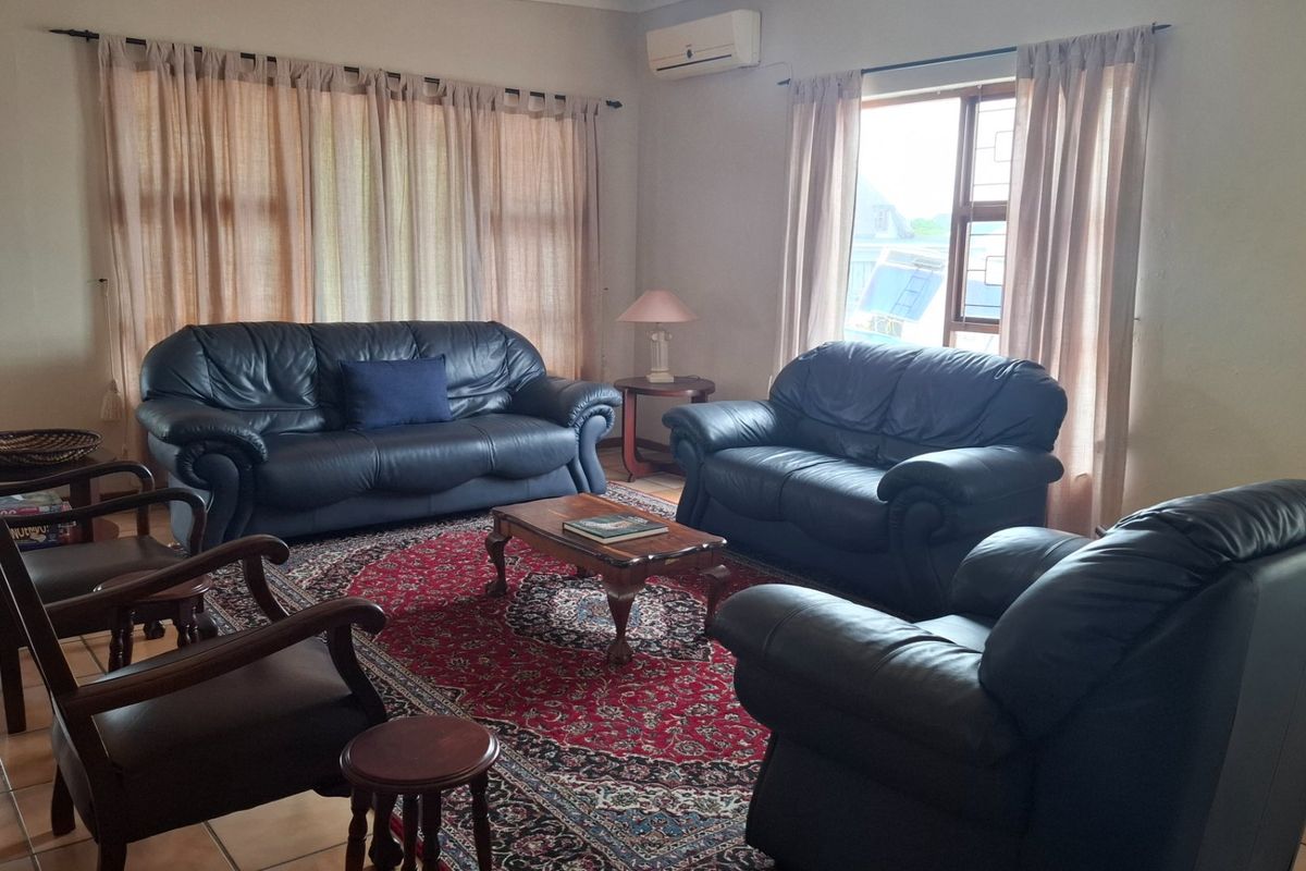 A spacious living room featuring tiled flooring, large windows with security bars, and a wall-mounted air conditioning unit.