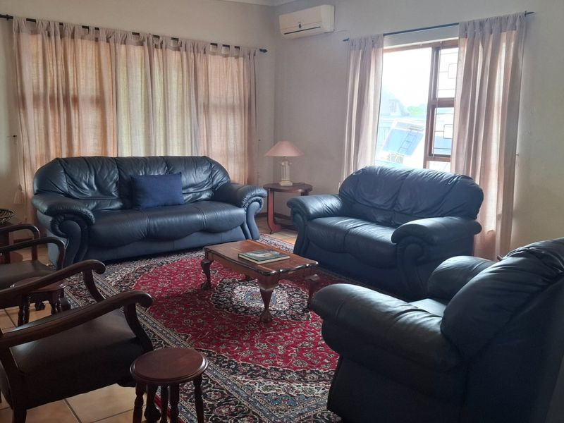A spacious living room featuring tiled flooring, large windows with security bars, and a wall-mounted air conditioning unit.