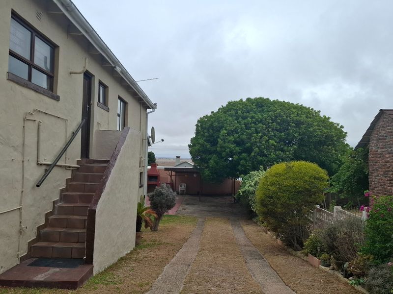 Rear exterior view of the property featuring an external staircase, concrete driveway, and established garden area with boundary walling.