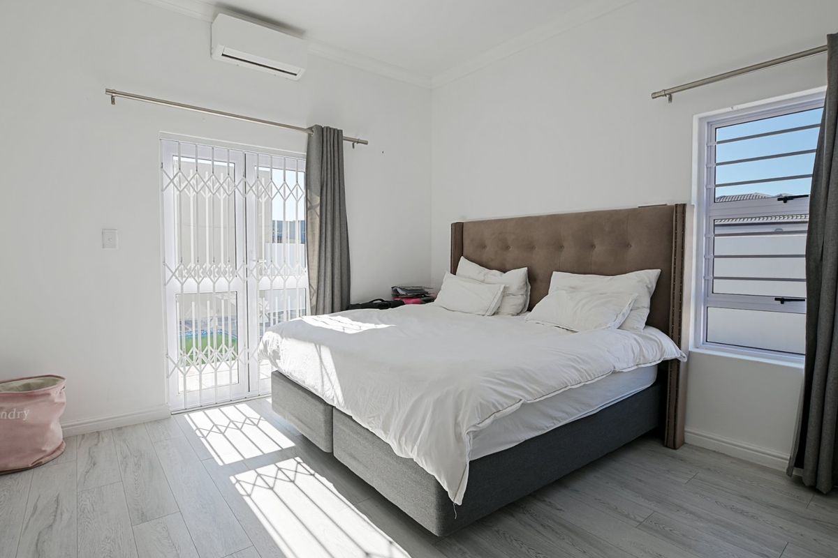 A bright bedroom featuring laminate flooring, a wall-mounted air conditioning unit, and a security gate providing access to the exterior.