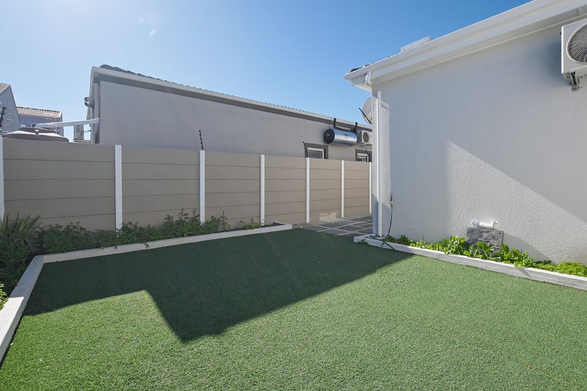 A neat, low-maintenance rear garden featuring artificial turf, a paved walkway, and secure boundary walling with electric fencing.