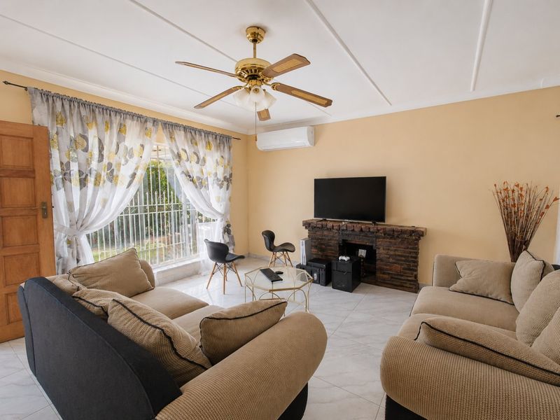 A comfortable living room featuring a brick fireplace, ceiling fan, split-system air conditioning, and tiled flooring with access to an outdoor area.