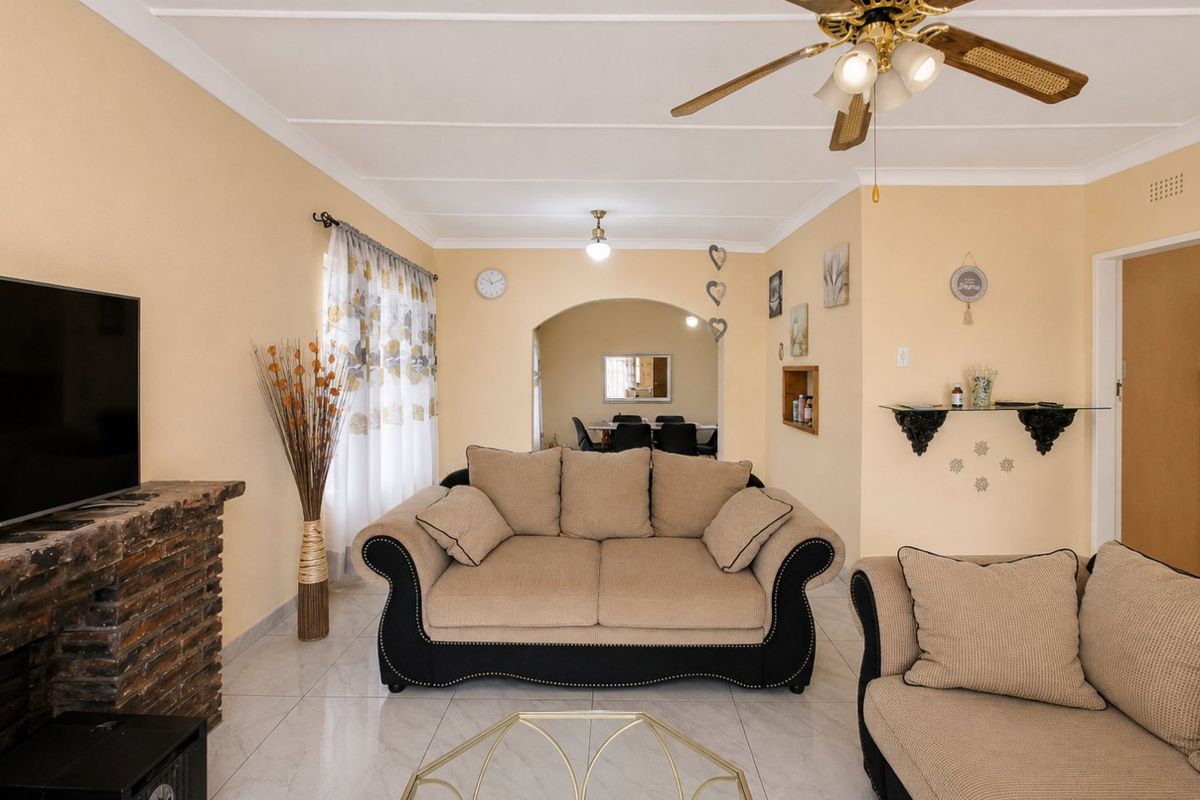 A comfortable living room featuring a brick fireplace, tiled flooring, and a ceiling fan, with an open archway leading to the dining area.