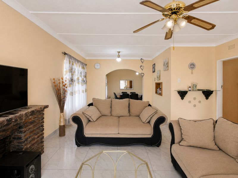 A comfortable living room featuring a brick fireplace, tiled flooring, and a ceiling fan, with an open archway leading to the dining area.