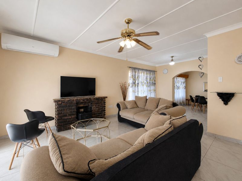 Spacious living room featuring a brick fireplace, ceiling fan, and split-system air conditioning, with an open-plan flow leading to the dining area.