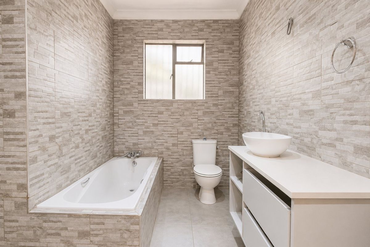 A modern bathroom featuring floor-to-ceiling textured stone-look wall tiles, a built-in bathtub, a vanity with a vessel sink, and a toilet.