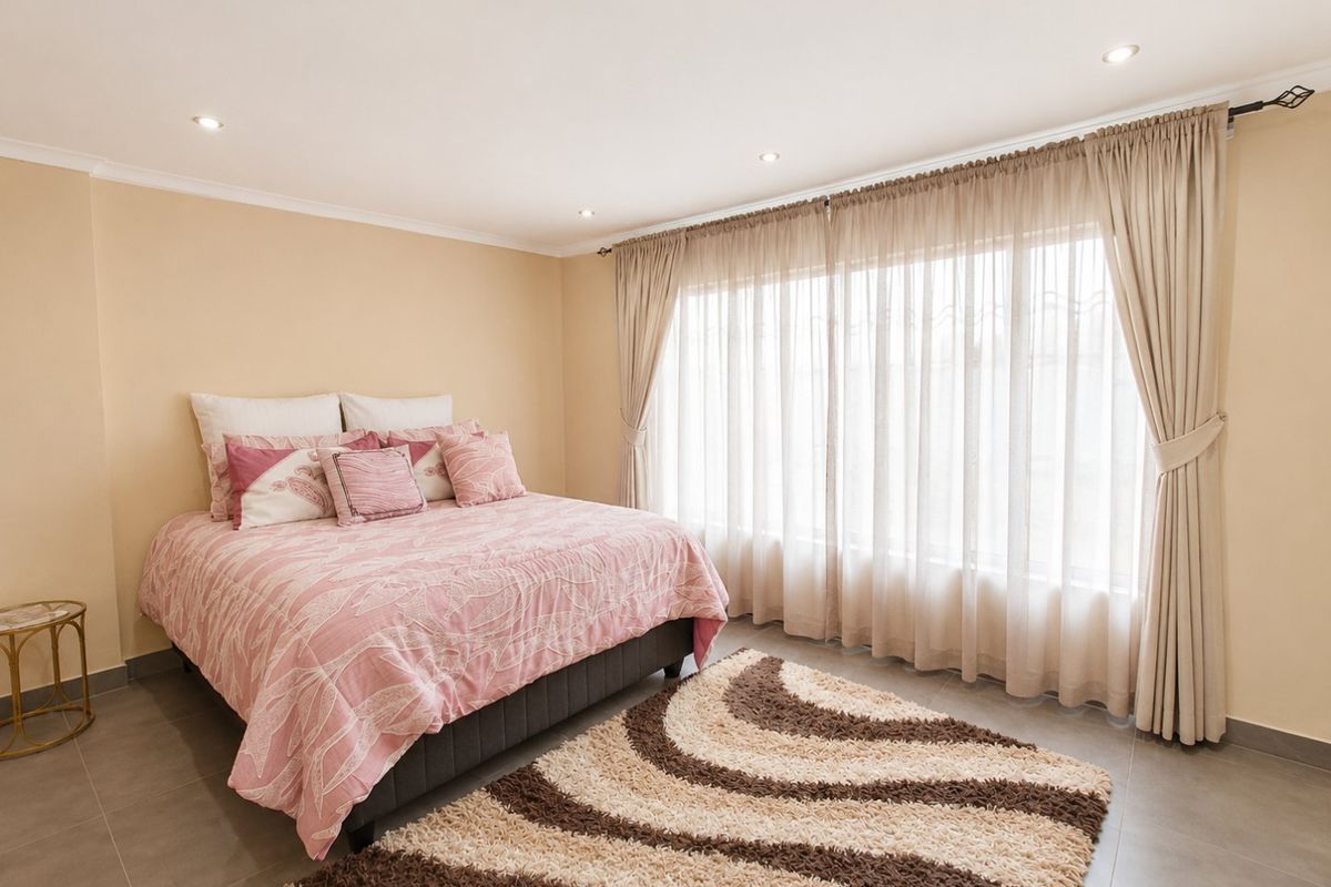 A well-maintained bedroom featuring neutral wall tones, large windows with curtain tracks, recessed downlighting, and durable tiled flooring.