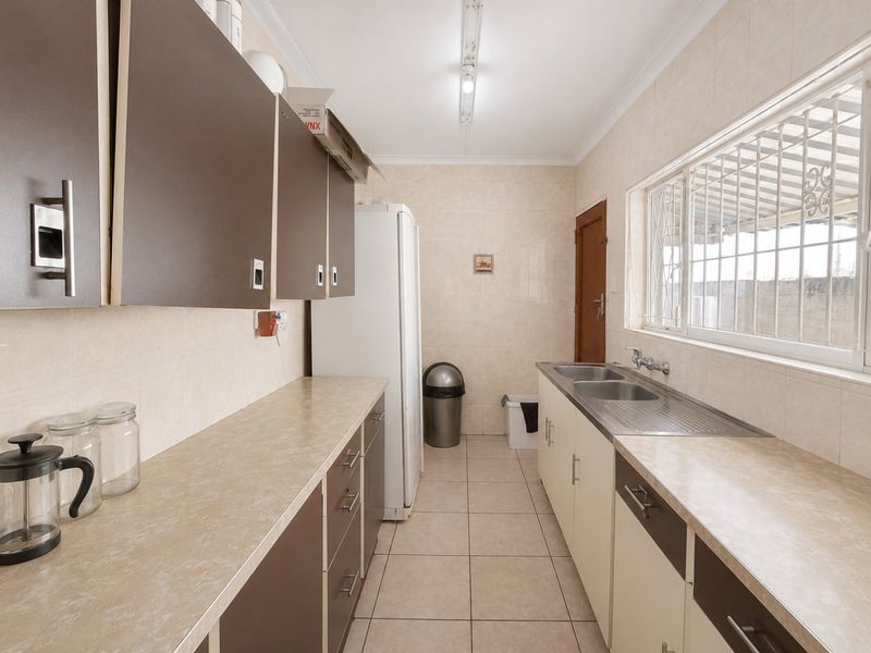 A functional galley-style kitchen featuring tiled flooring, neutral wall tiles, laminate countertops, and ample built-in cabinetry with a double stainless steel sink.