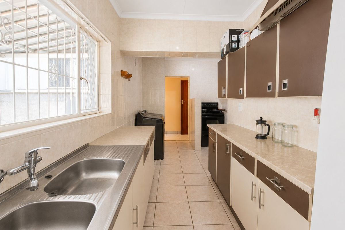 A functional kitchen featuring double stainless steel sinks, laminate countertops, two-tone cabinetry, and tiled finishes, with an adjacent utility area.
