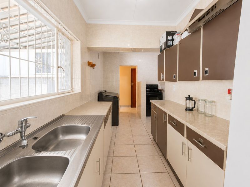 A functional kitchen featuring double stainless steel sinks, laminate countertops, two-tone cabinetry, and tiled finishes, with an adjacent utility area.