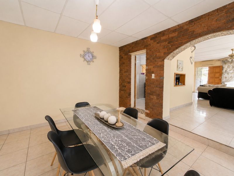 Dining area featuring ceramic floor tiles, an exposed brick archway leading to adjacent living spaces, and a suspended ceiling.