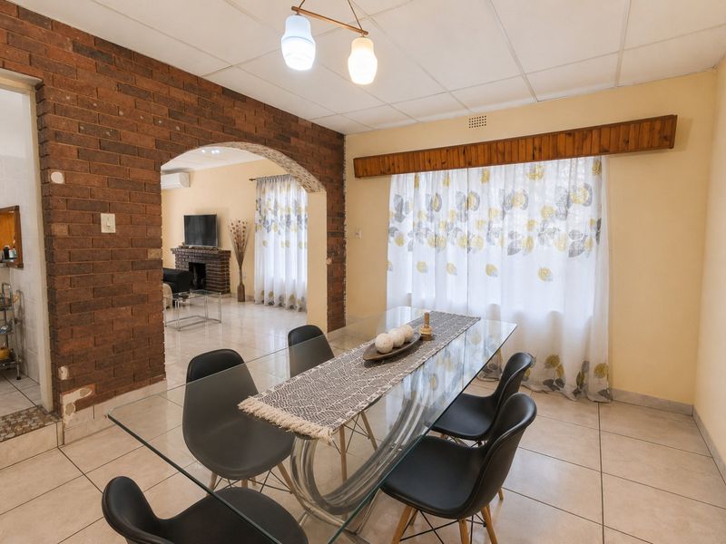 Dining area featuring an exposed brick archway, tiled flooring, and a drop ceiling, connecting to an adjacent living space.