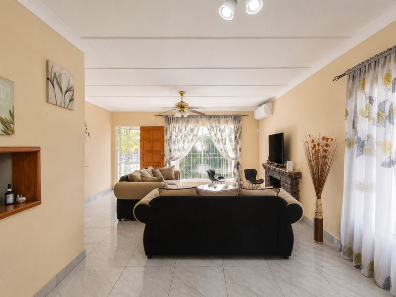 Spacious living room featuring tiled flooring, a brick fireplace, ceiling fan, and split-system air conditioning, offering a comfortable and functional layout.