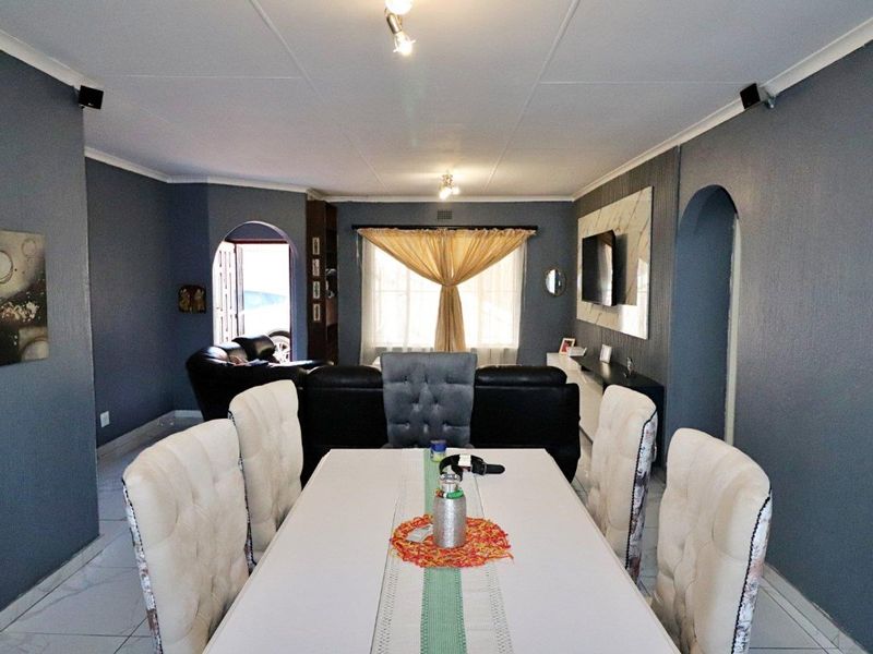 Open plan living and dining area featuring tiled flooring, arched doorways, and a modern feature wall with integrated television mounting.