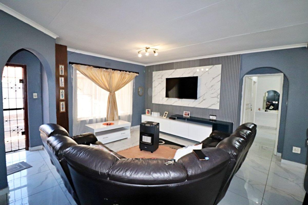 A well-maintained living room featuring a modern marble-effect feature wall with integrated slatted paneling, tiled flooring, and an elegant arched entryway.