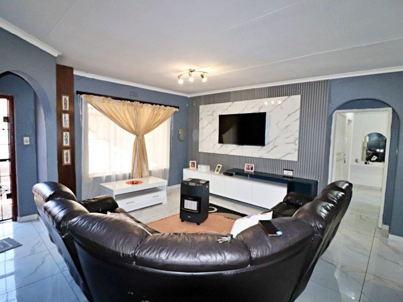 A well-maintained living room featuring a modern marble-effect feature wall with integrated slatted paneling, tiled flooring, and an elegant arched entryway.