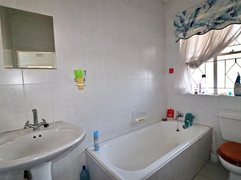 A functional bathroom featuring a pedestal basin, bathtub, and toilet with tiled walls and a window with security bars.
