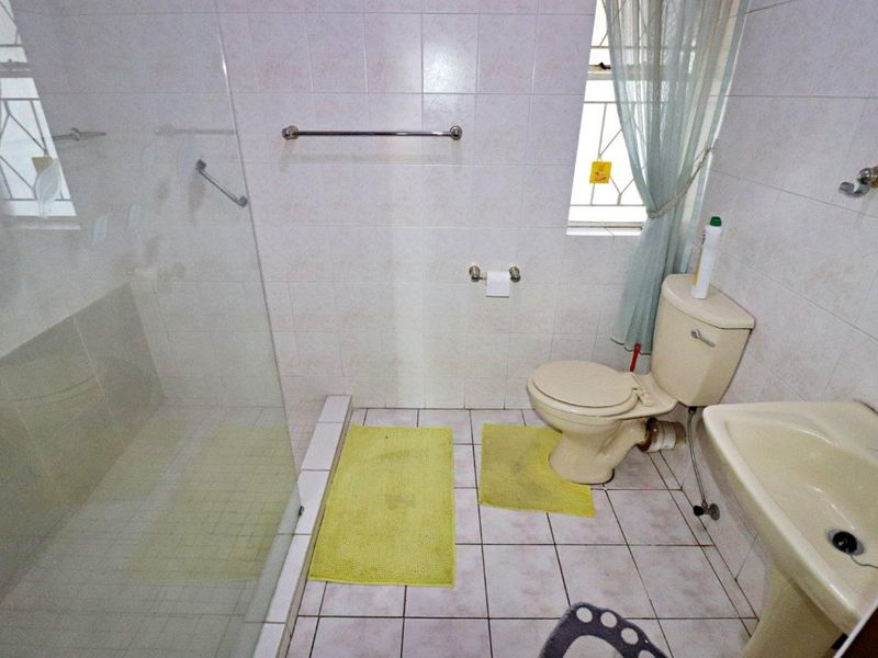 A functional bathroom featuring a glass shower enclosure, pedestal basin, and toilet with neutral wall and floor tiling.