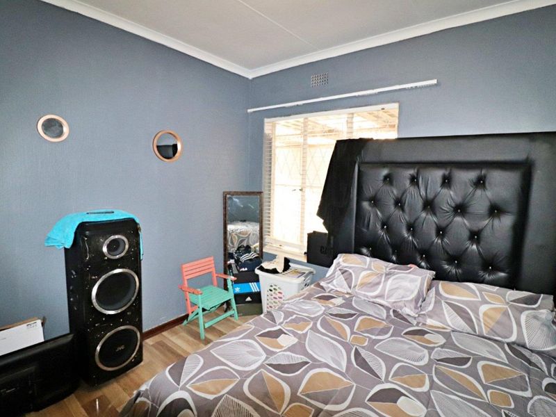 A bedroom featuring laminate flooring, blue painted walls, and a window fitted with security bars.
