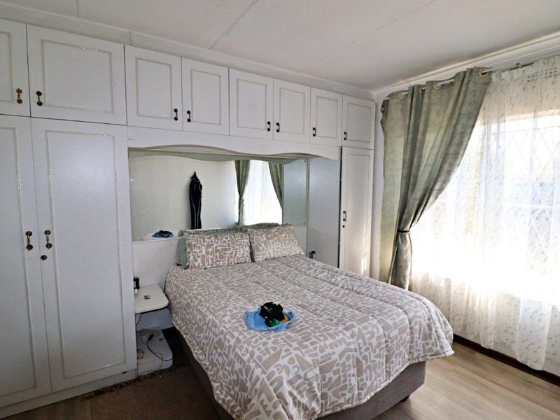 A bedroom featuring extensive built-in cabinetry with integrated mirrored headboard and light-toned laminate flooring.