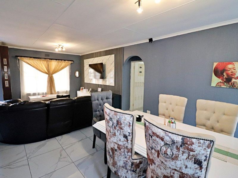 Open plan living and dining area featuring large format floor tiles, a decorative feature wall, and an arched doorway leading to adjacent rooms.