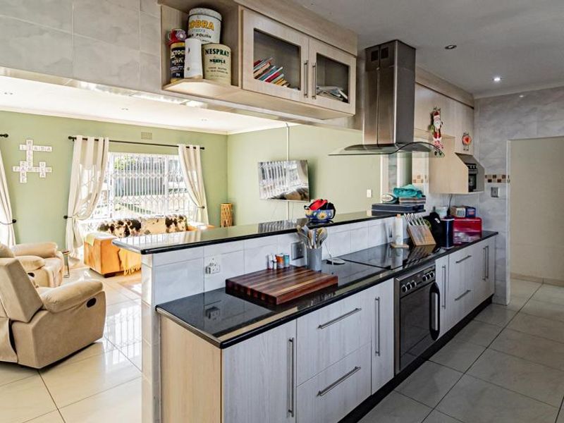 Open-plan kitchen and living area featuring granite countertops, built-in oven, stainless steel extractor fan, and tiled flooring throughout.