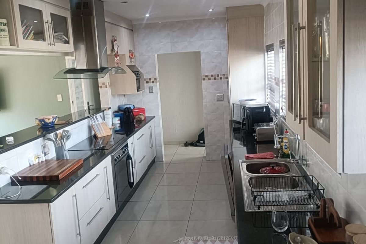 A functional galley-style kitchen featuring light wood cabinetry, dark granite countertops, stainless steel extractor fan, and tiled flooring with recessed lighting.