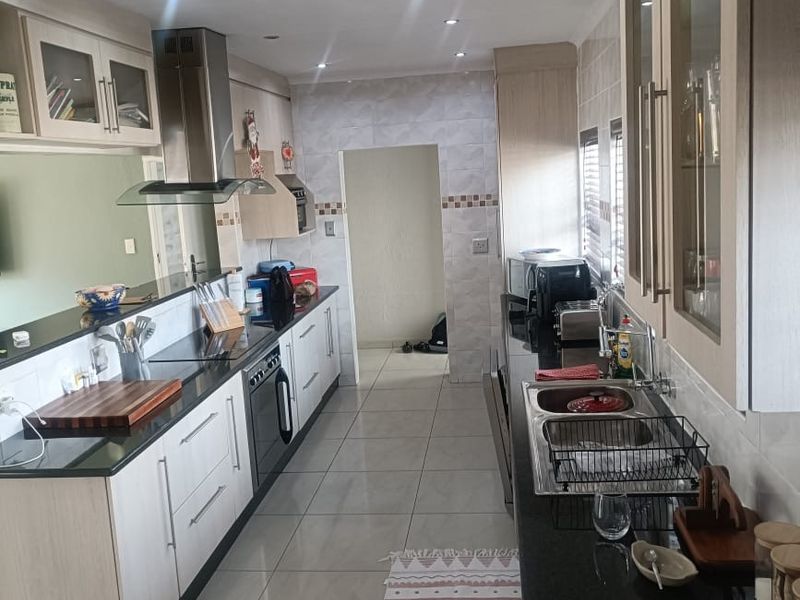 A functional galley-style kitchen featuring light wood cabinetry, dark granite countertops, stainless steel extractor fan, and tiled flooring with recessed lighting.